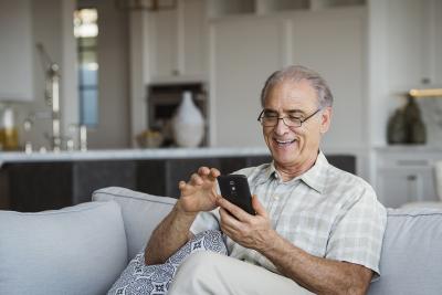 A man sitting on his couch, smiling at his phone screen